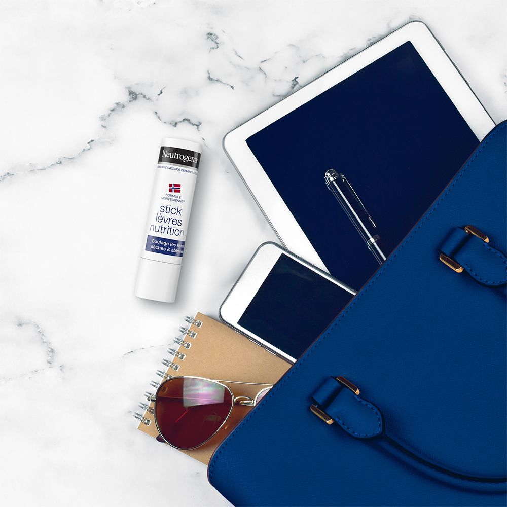 Stick labbra Neutrogena in borsa blu con tablet, telefono, penna e occhiali da sole.