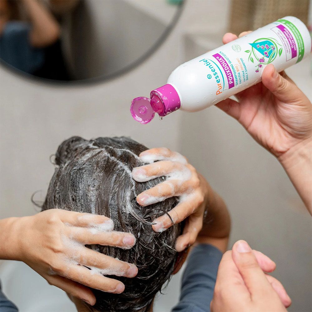 Persona che si lava i capelli con lo shampoo. Flacone con tappo viola. Scritta: Puressentiel Poudoux®.