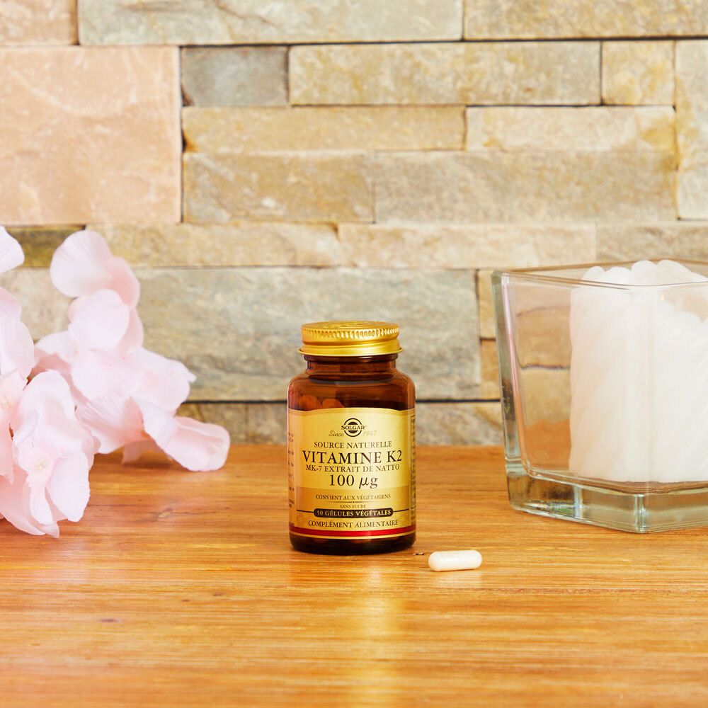 Flacone dorato su legno, una capsula accanto. Sfondo: muro in pietra.