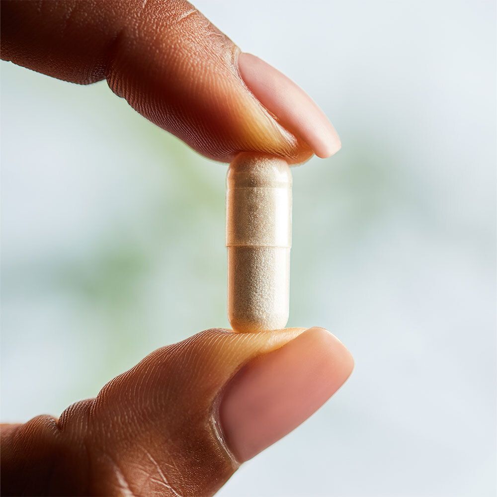 Una capsula tenuta tra due dita. Color crema.