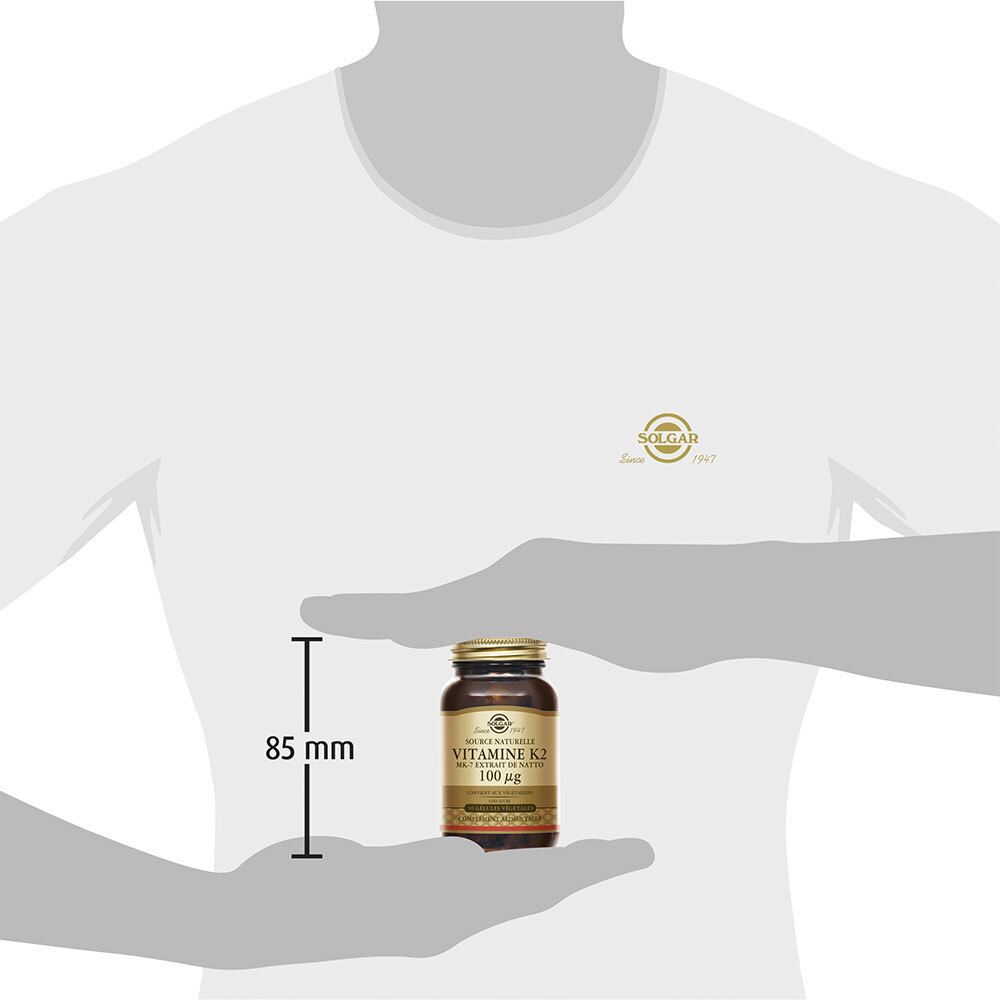 Uomo tiene flacone. Sul flacone: Vitamina K2 100 µg. Dimensioni: 85 mm.