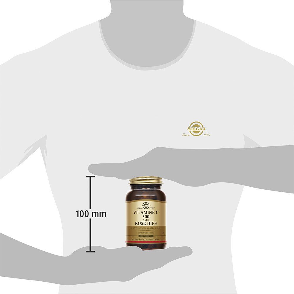 Persona che tiene in mano un flacone di vetro marrone. Il flacone è alto 100 mm. Sul flacone: Vitamina C 500 con rosa canina.