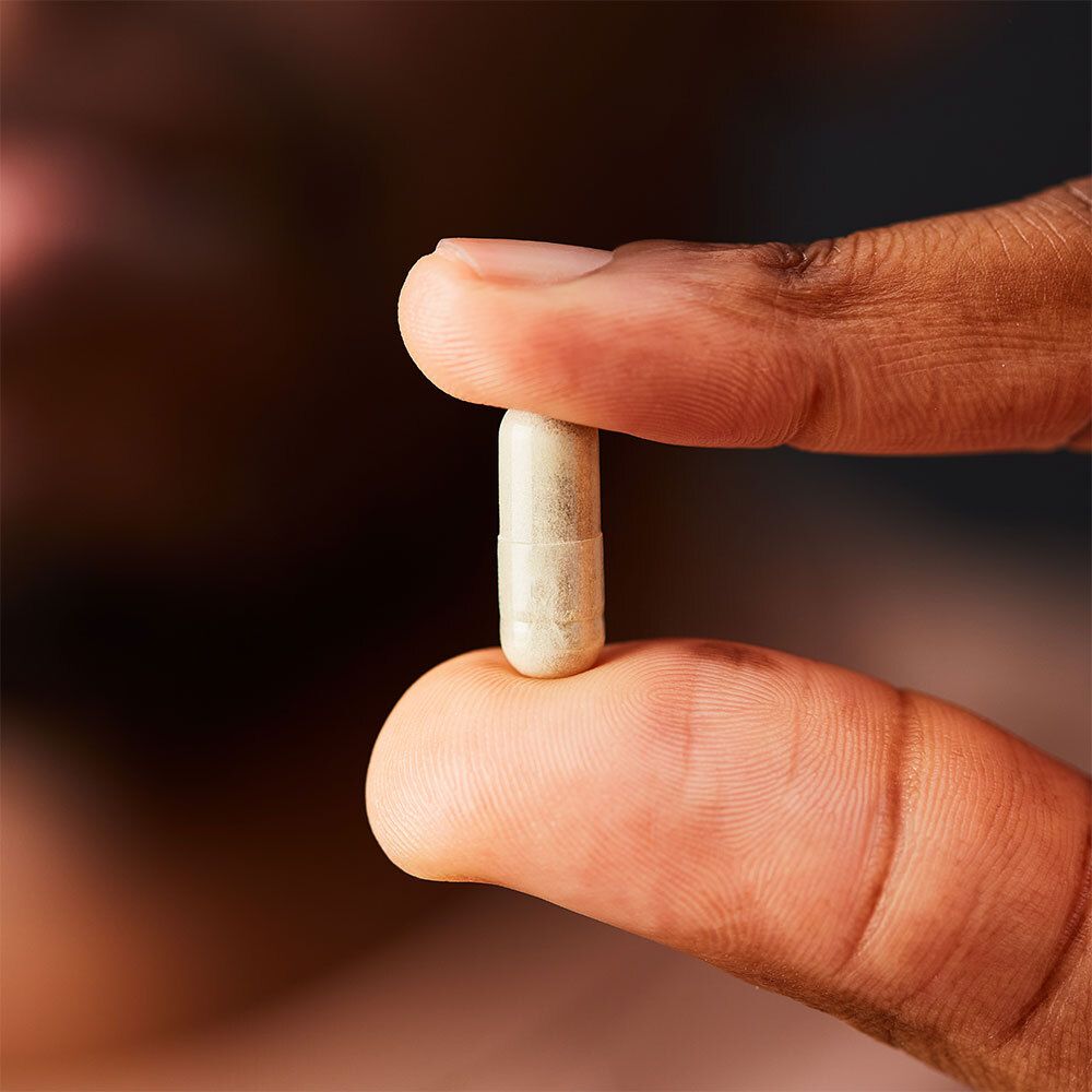 Persona che tiene una singola capsula di vitamina C tra le dita.