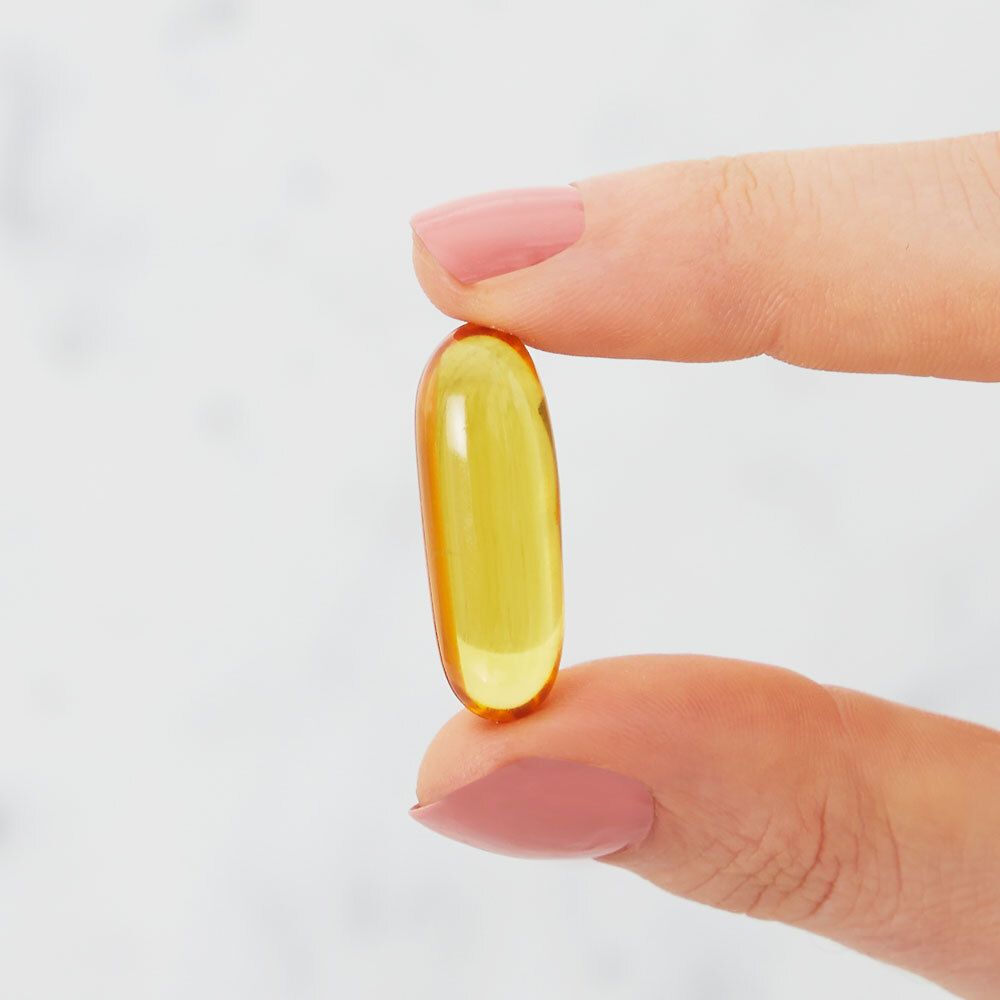 Capsula ovale gialla tenuta tra due dita. Su sfondo chiaro.