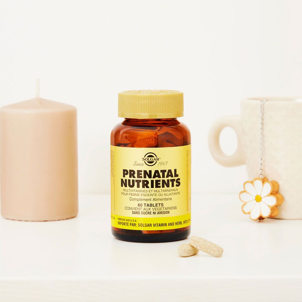 Flacone di vetro marrone con tappo dorato e due compresse. Scritta: Solgar Prenatal Nutrients. Su tavolo con candela e tazza.