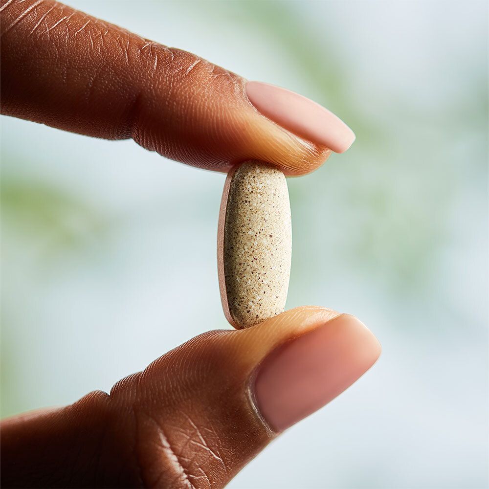 Una compressa ovale beige tenuta tra due dita. Nessuna scritta visibile.