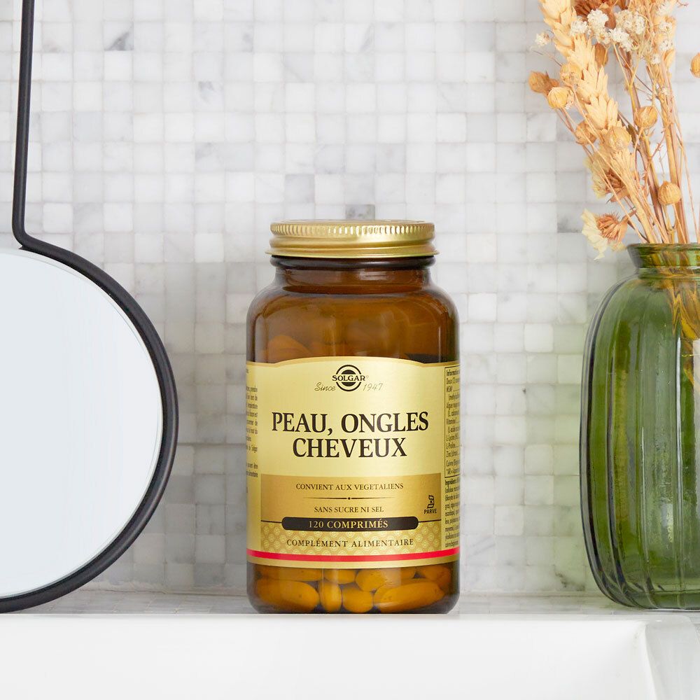 Flacone di vetro con tappo dorato. Scritta « Peau, Ongles, Cheveux ». Appoggiato su una superficie bianca.