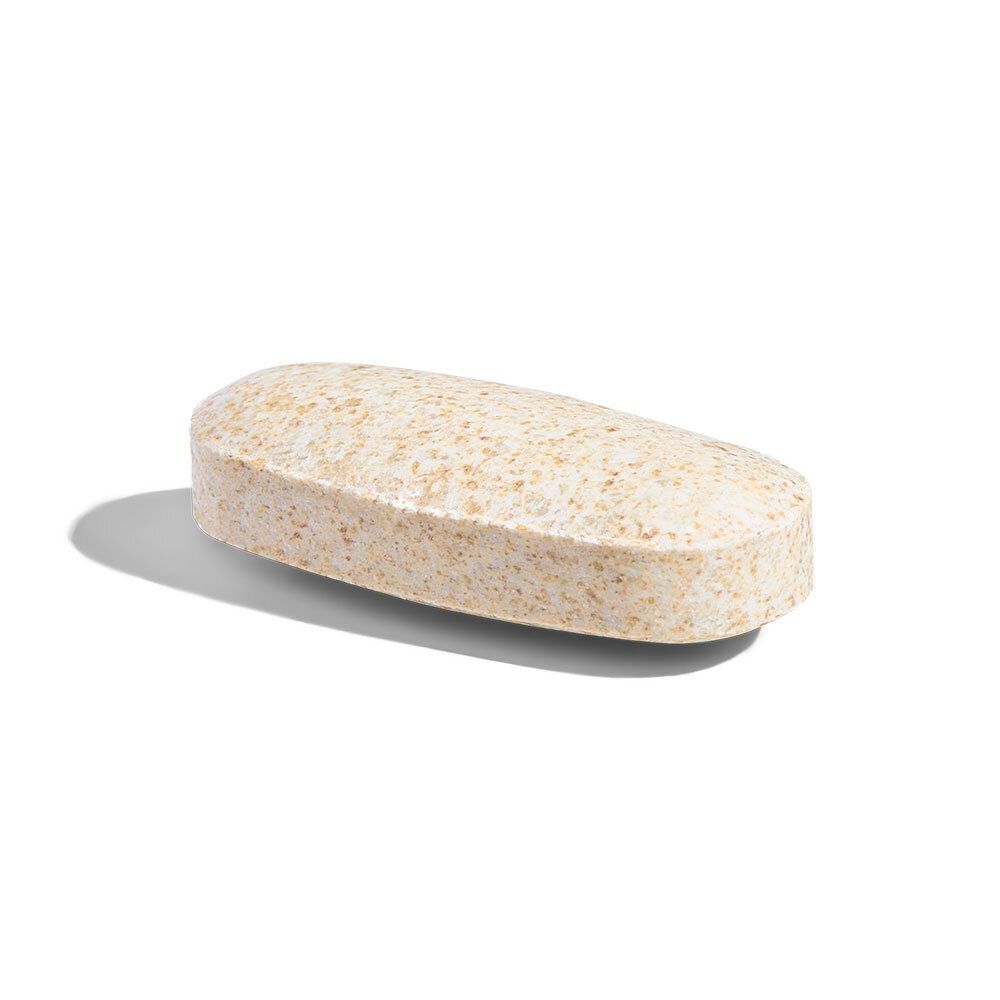 Un'unica compressa oblunga. Colore beige. Appoggiata su una superficie bianca.