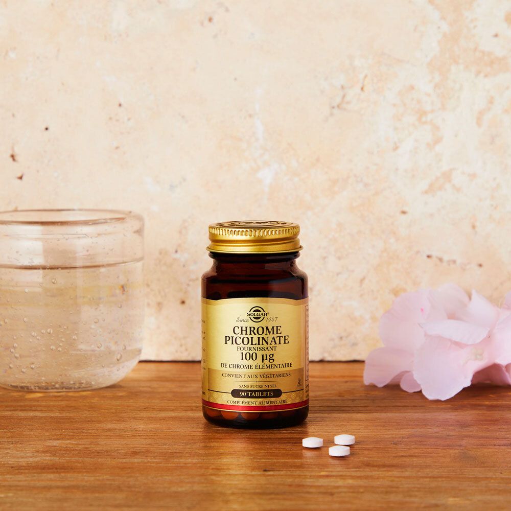 Flacone marrone con compresse su superficie in legno. Bicchiere d'acqua e fiore sullo sfondo.