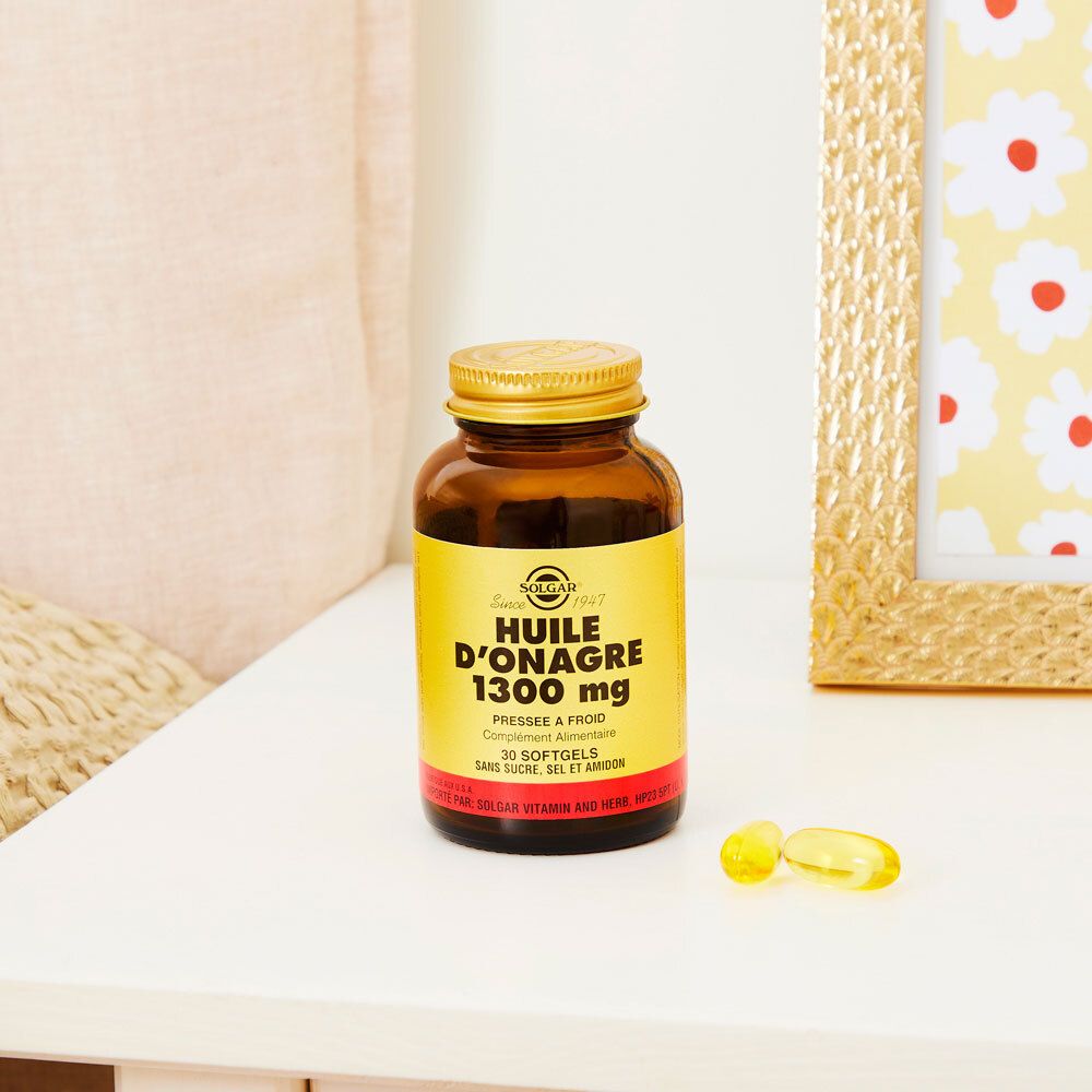 Flacone marrone, tappo dorato. Due capsule accanto. Su un tavolo, vicino a una cornice.