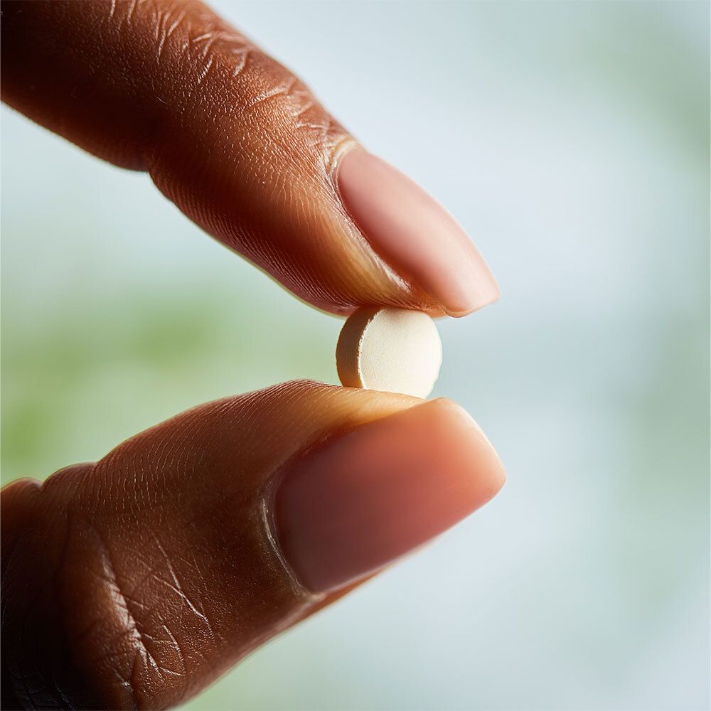 Mano che tiene una singola compressa rotonda bianca tra le dita.