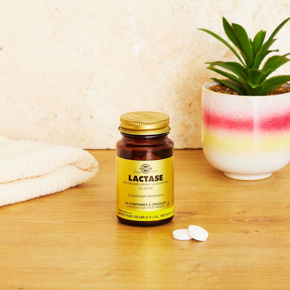 Flacone di vetro marrone con tappo dorato ed etichetta. Due compresse accanto. Sfondo: tavolo e pianta.