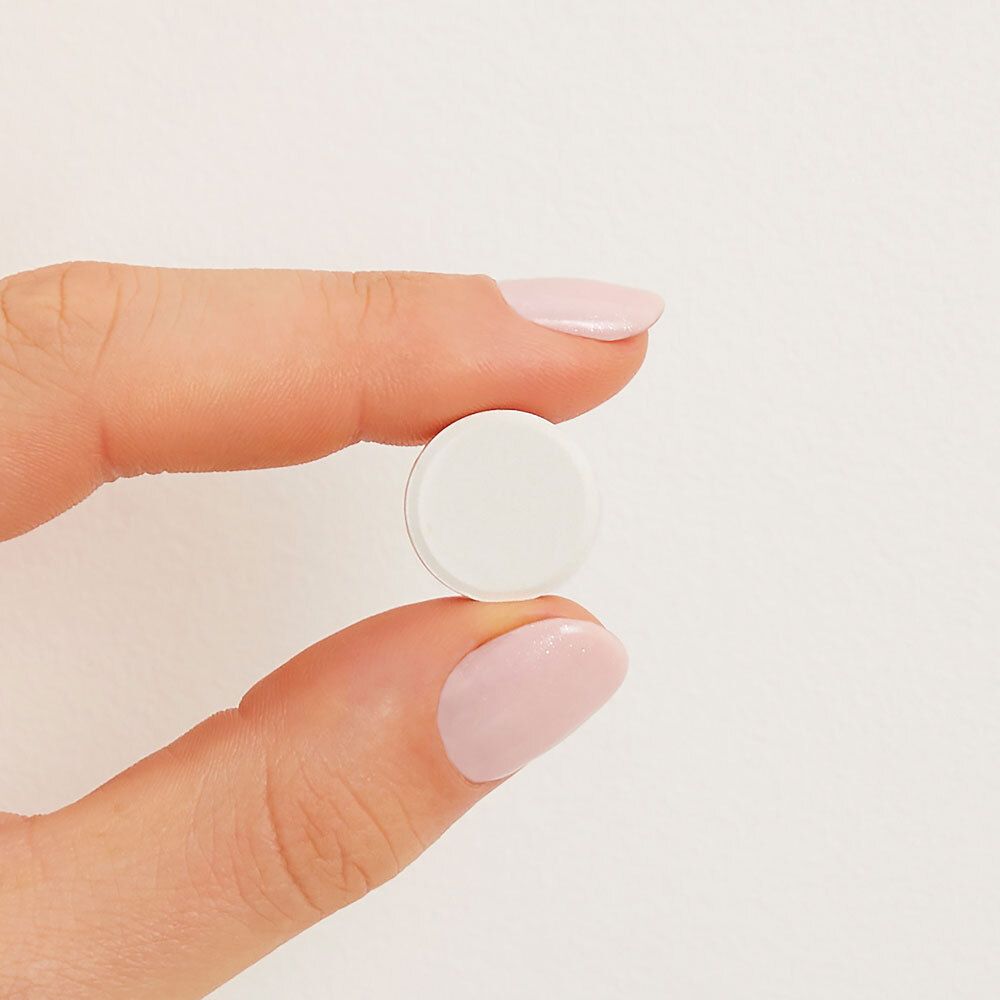 Una compressa, bianca e rotonda, tenuta in mano. Sfondo: bianco.