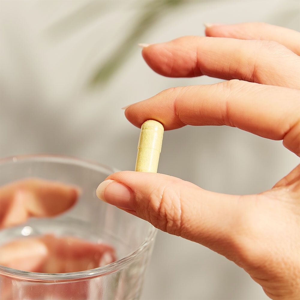 Mano che tiene una capsula gialla. Capsula in mano, davanti a un bicchiere d'acqua.
