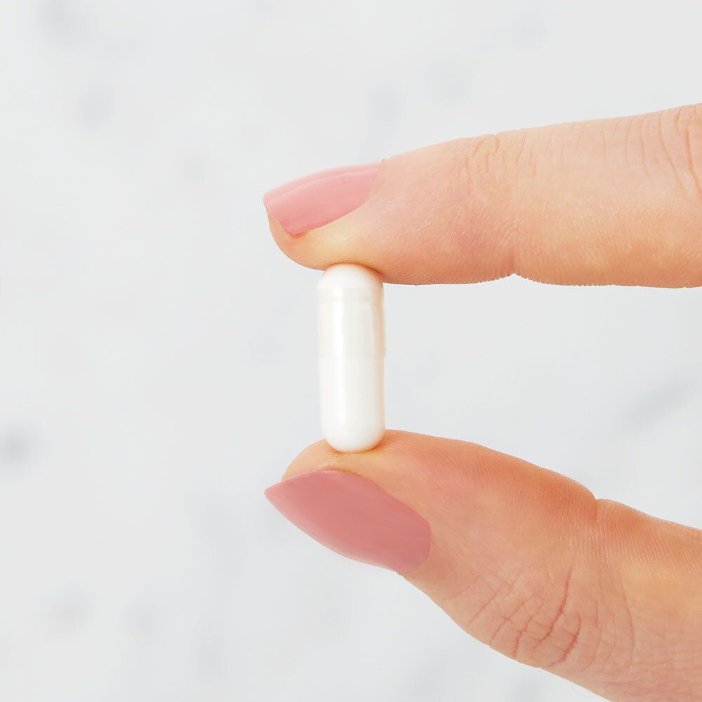 Una capsula bianca tra due dita. Unghie smaltate rosa.