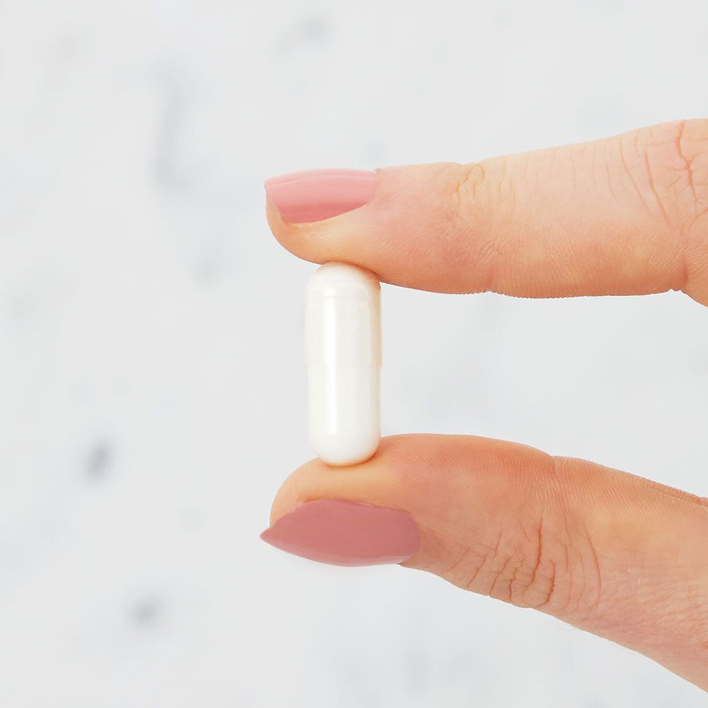 Una capsula bianca tra due dita. Sfondo sfocato.