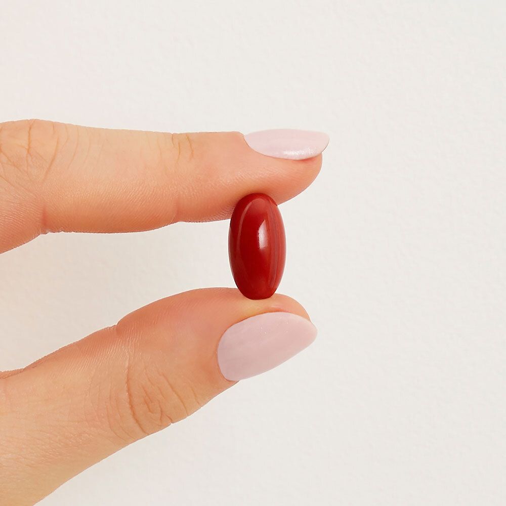 Una capsula rossa ovale, tenuta da una mano con unghie rosa smaltate.