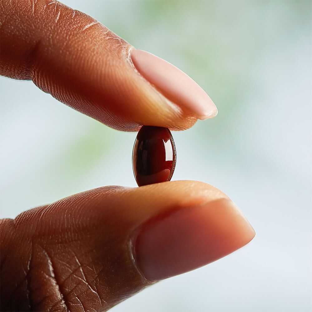 Dita che tengono una singola capsula softgel, rosso scuro.