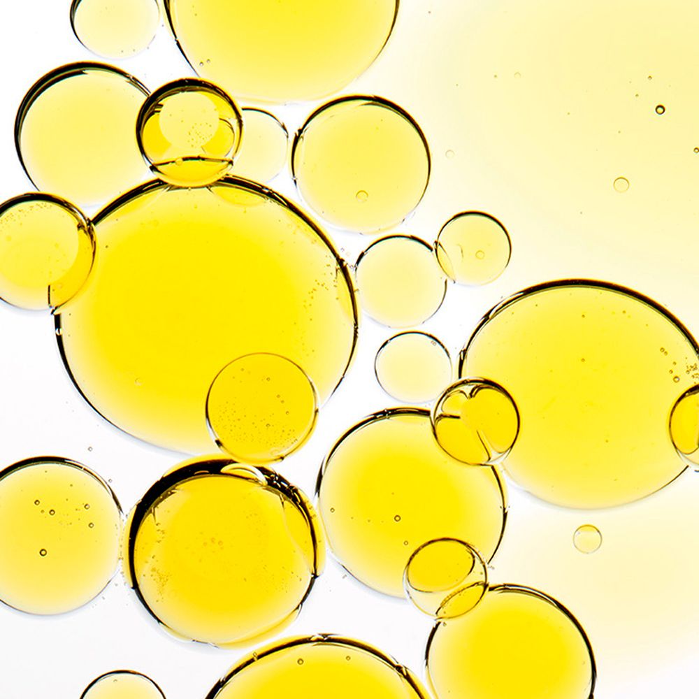 Primo piano di goccioline di olio giallo su sfondo bianco. Forme rotonde, dimensioni variabili.