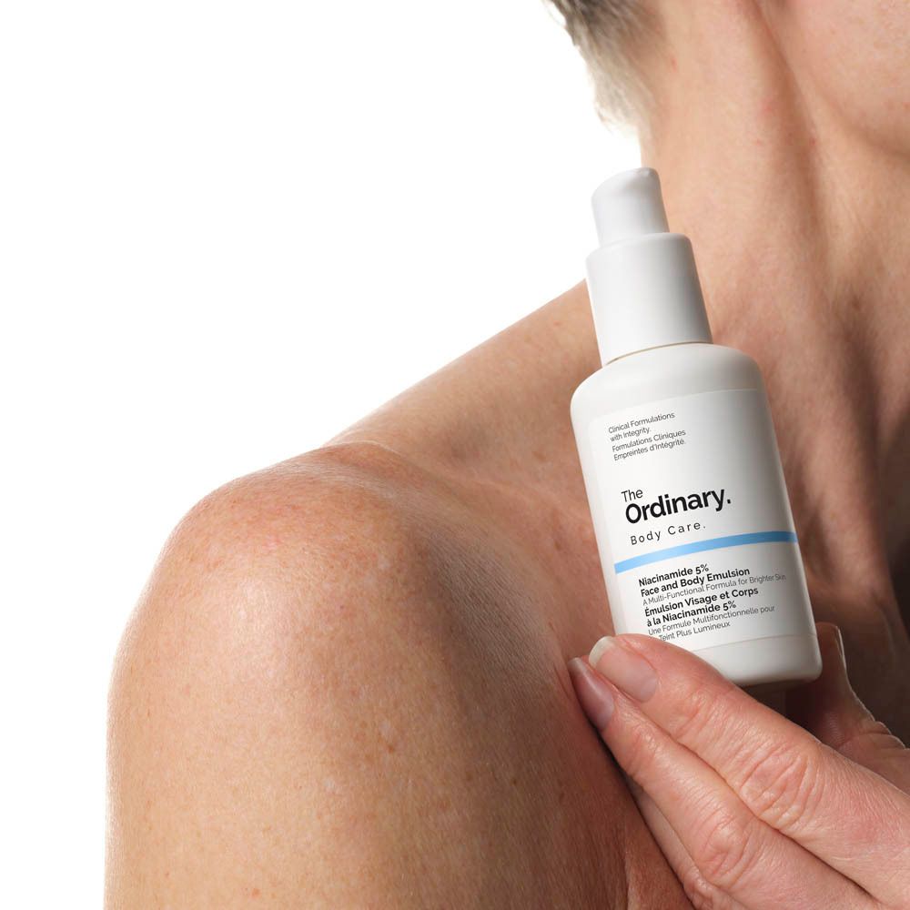 Flacone bianco con dosatore. Scritta: The Ordinary. Niacinamide 5% Face & Body Emulsion. Tenuto da una persona.