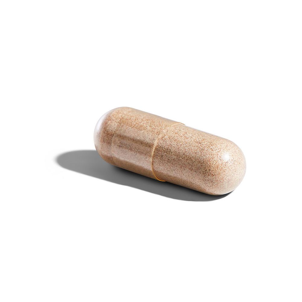 Una singola capsula oblunga. Capsula trasparente con contenuto marrone, su sfondo bianco.