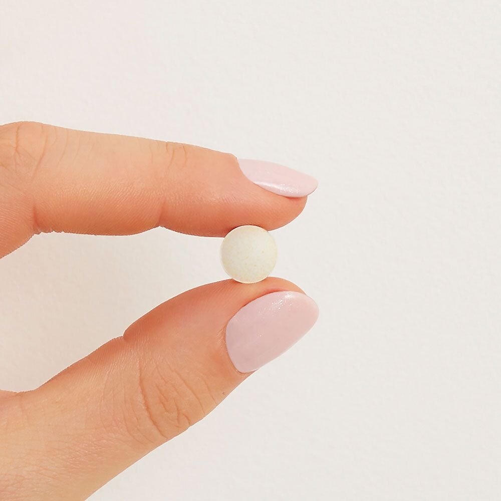 Una singola compressa rotonda bianca, tenuta da una mano con unghie smaltate di rosa.