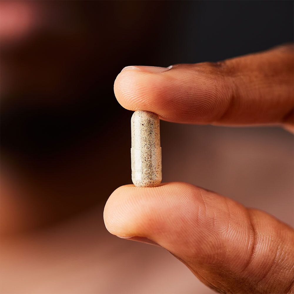 Una capsula tenuta tra due dita. Beige con punti scuri.