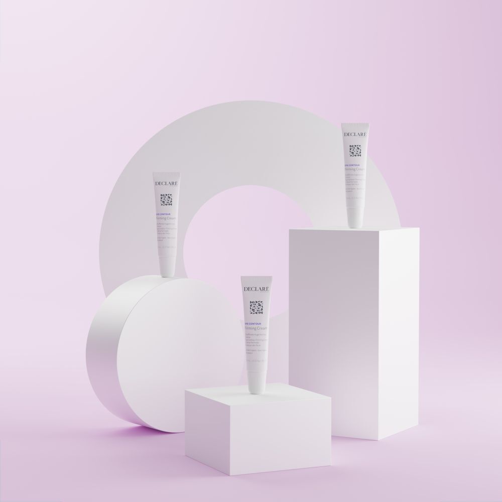 Tre tubi bianchi DECLARÉ Eye Contour Firming Cream su piedistalli. Sfondo con forme.