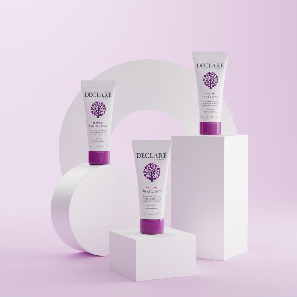 Tre tubi, tappi viola su piedistalli. DECLARÉ, Hand Cream, UV-Schutz Handcreme. Sfondo con forme.
