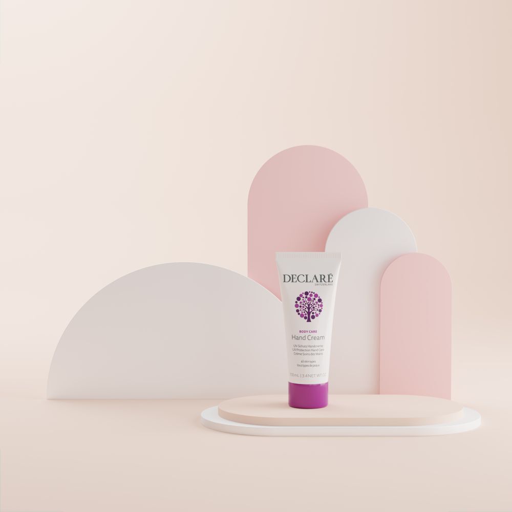 Tubo bianco, tappo viola su piedistallo. DECLARÉ, Hand Cream, UV-Schutz Handcreme. Sfondo con forme.