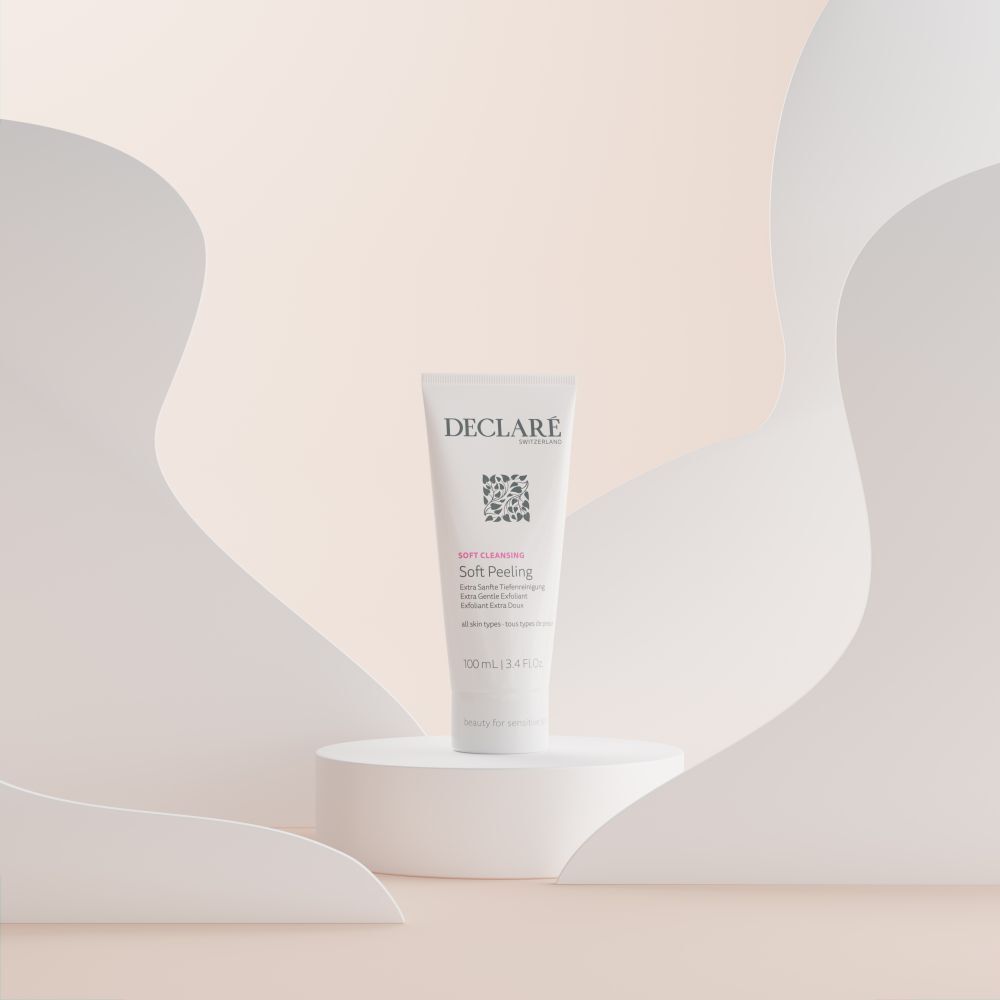 Tubo bianco DECLARÉ Soft Peeling su piedistallo. Sfondo con forme curve pastello.