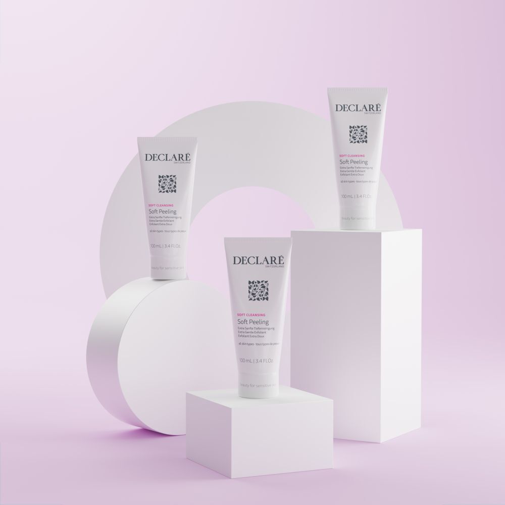 Tre tubi DECLARÉ Soft Peeling su piedistalli. Sfondo pastello con forme geometriche.