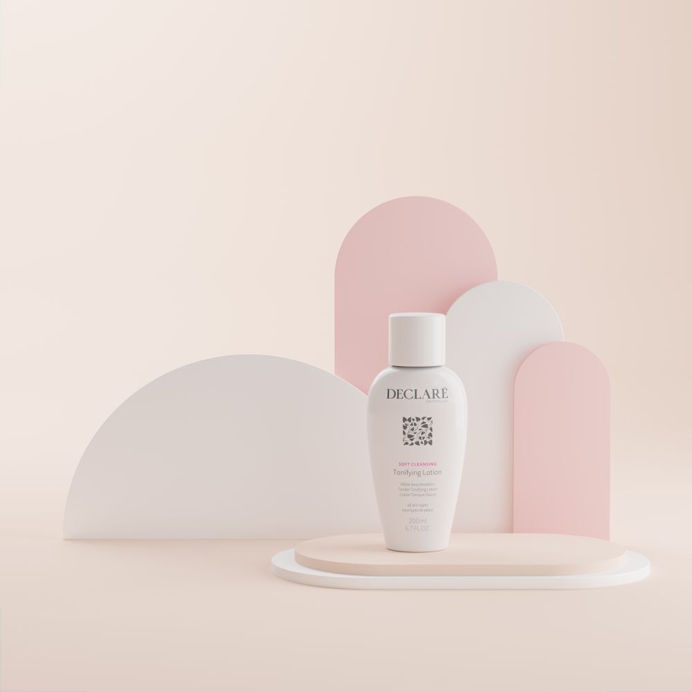 Flacone bianco DECLARÉ Toning Lotion su piedistallo. Scritta: Soft Cleansing, Toning Lotion. Sfondo: forme rosa.