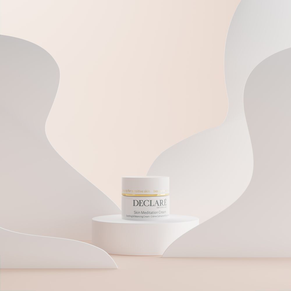 Vasetto di crema bianco su piedistallo. Sfondo con elementi ondulati bianchi. Scritta: DECLARÉ Skin Meditation Cream.