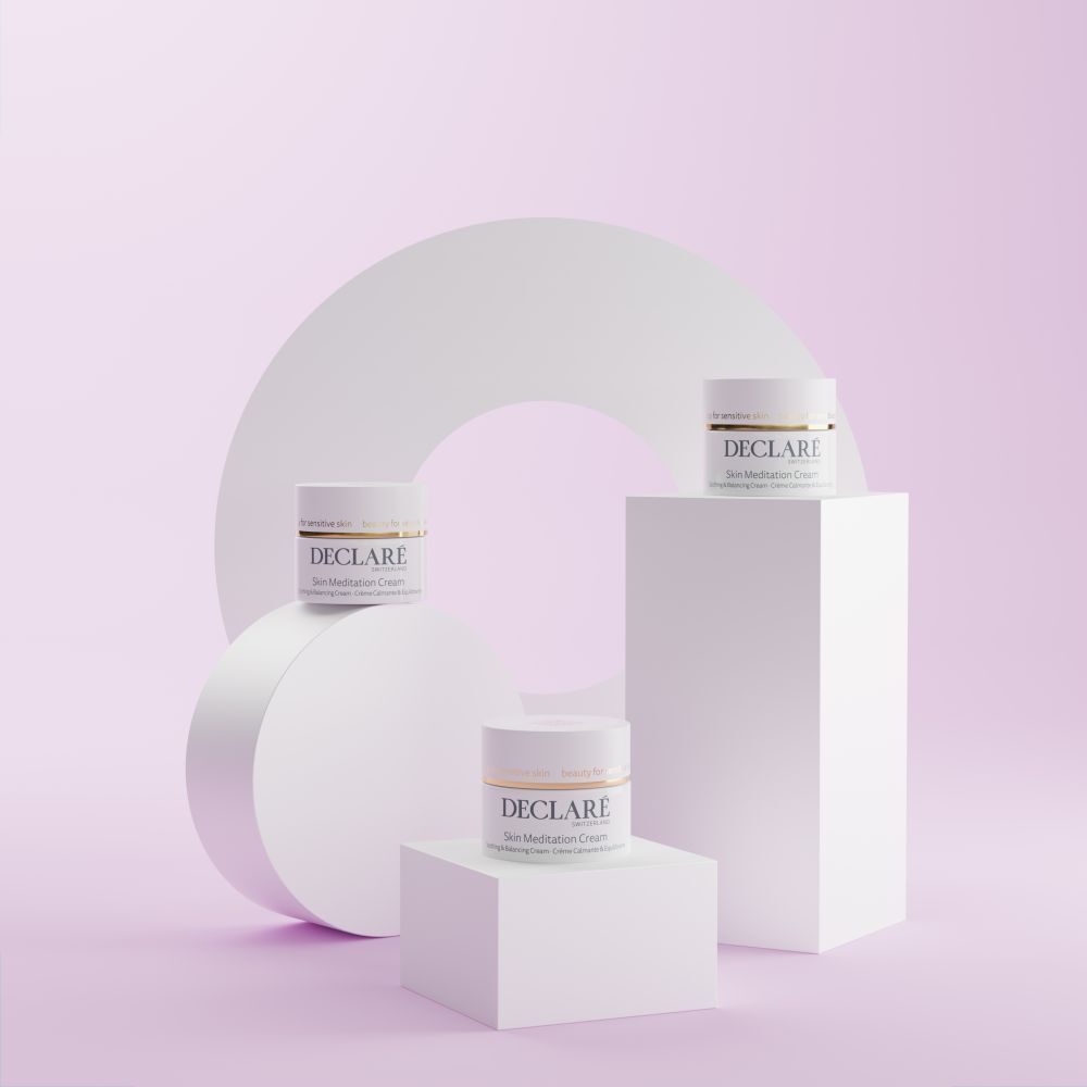 Tre vasetti di crema su piedistalli. Sfondo con cerchio bianco ed elementi rosa. Scritta: DECLARÉ Skin Meditation Cream.