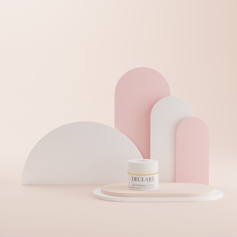 Vasetto di crema su piedistallo. Sfondo con elementi bianchi e rosa. Scritta: DECLARÉ Skin Meditation Cream.