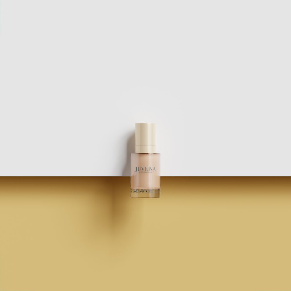 Fluido colorato Juvena of Switzerland. Flacone beige, tappo dorato. Su sfondo chiaro.