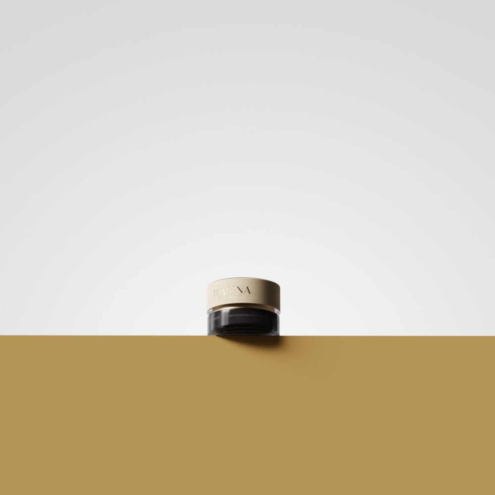 Vaso di crema con coperchio dorato. Scritta: JUVENA. Posizionato su superficie dorata. Sfondo: giallo e bianco.