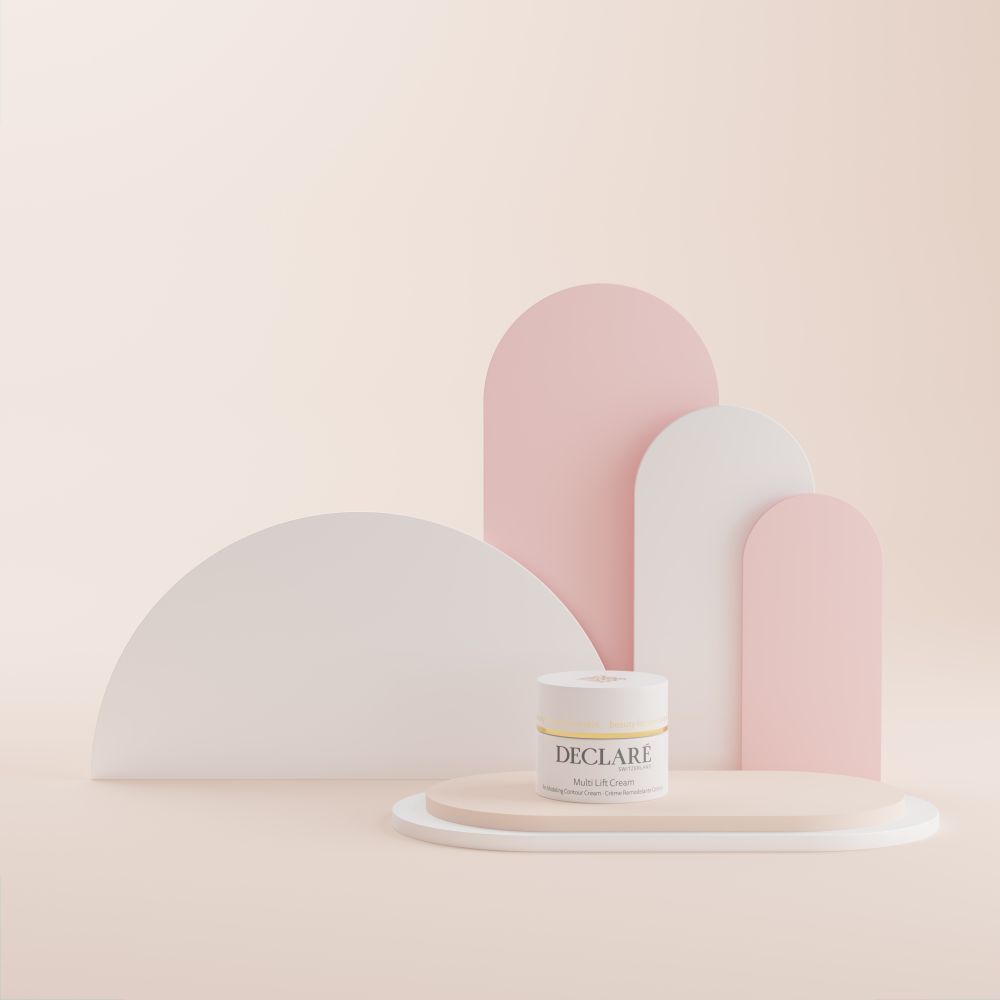 Vasetto di crema su piedistallo. DECLARÉ Multi Lift Cream. Sfondo con forme bianche e rosa.