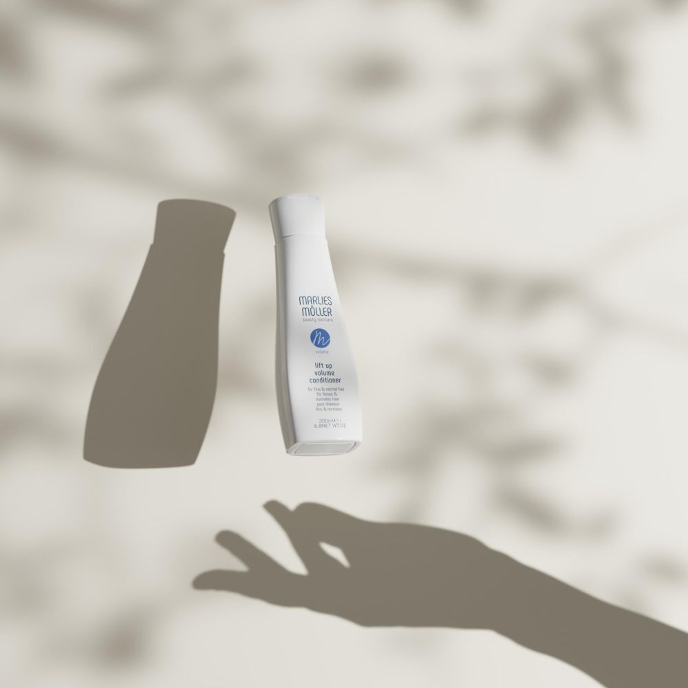 Flacone Marlies Möller Volume Conditioner e ombra su sfondo chiaro. Ombra della mano.