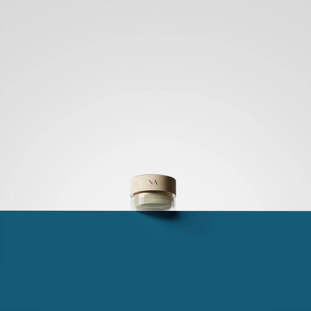 Piccolo vasetto di crema con coperchio dorato. Scritta: Juvena. Su sfondo blu e bianco.