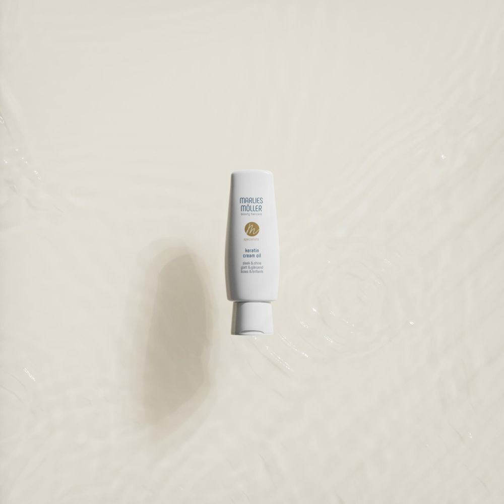 Flacone bianco Marlies Möller Keratin Cream Oil in acqua. Nome del prodotto, logo e scritta. Liscio e lucente.