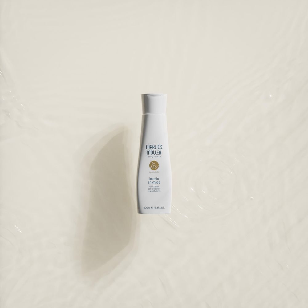 Flacone di shampoo Marlies Möller Keratin su sfondo beige. Flacone con tappo bianco ed etichetta.