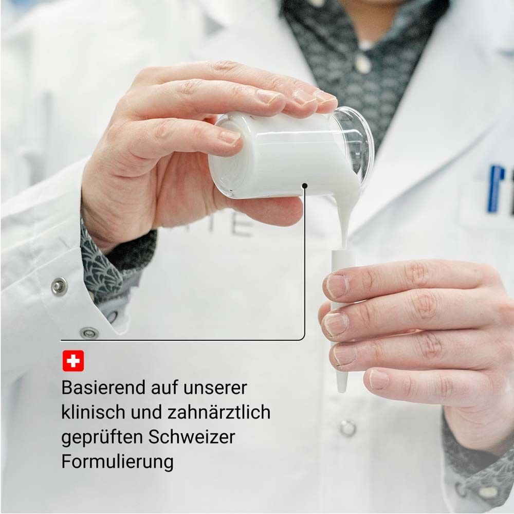 Mani che versano un liquido in un piccolo contenitore. Testo: Formulazione svizzera clinicamente testata e dai dentisti.