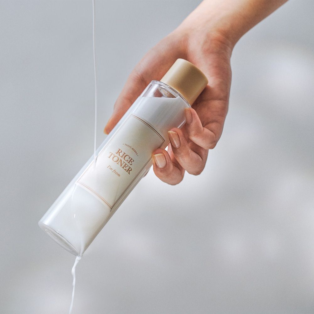 Mano che tiene una bottiglia trasparente di liquido bianco con etichetta 'RICE TONER'.