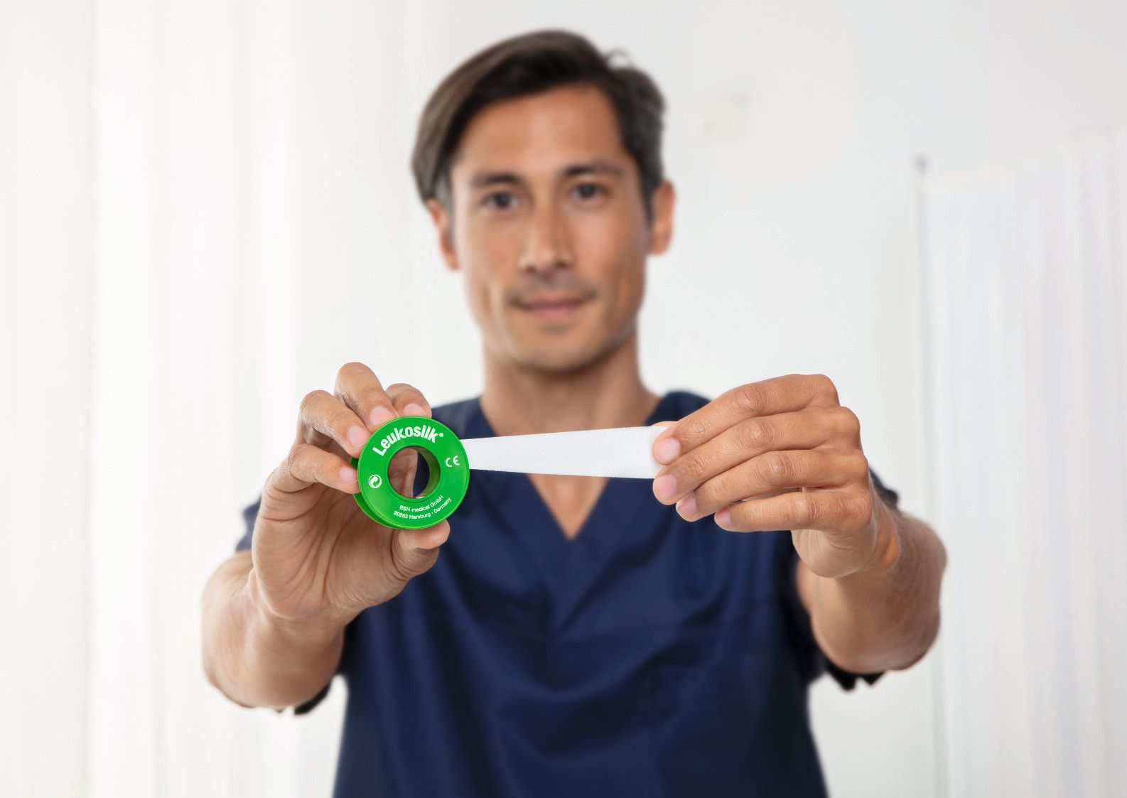 Uomo che tiene in mano un rotolo di nastro adesivo e tira il nastro. Scritta: Leukosilk.