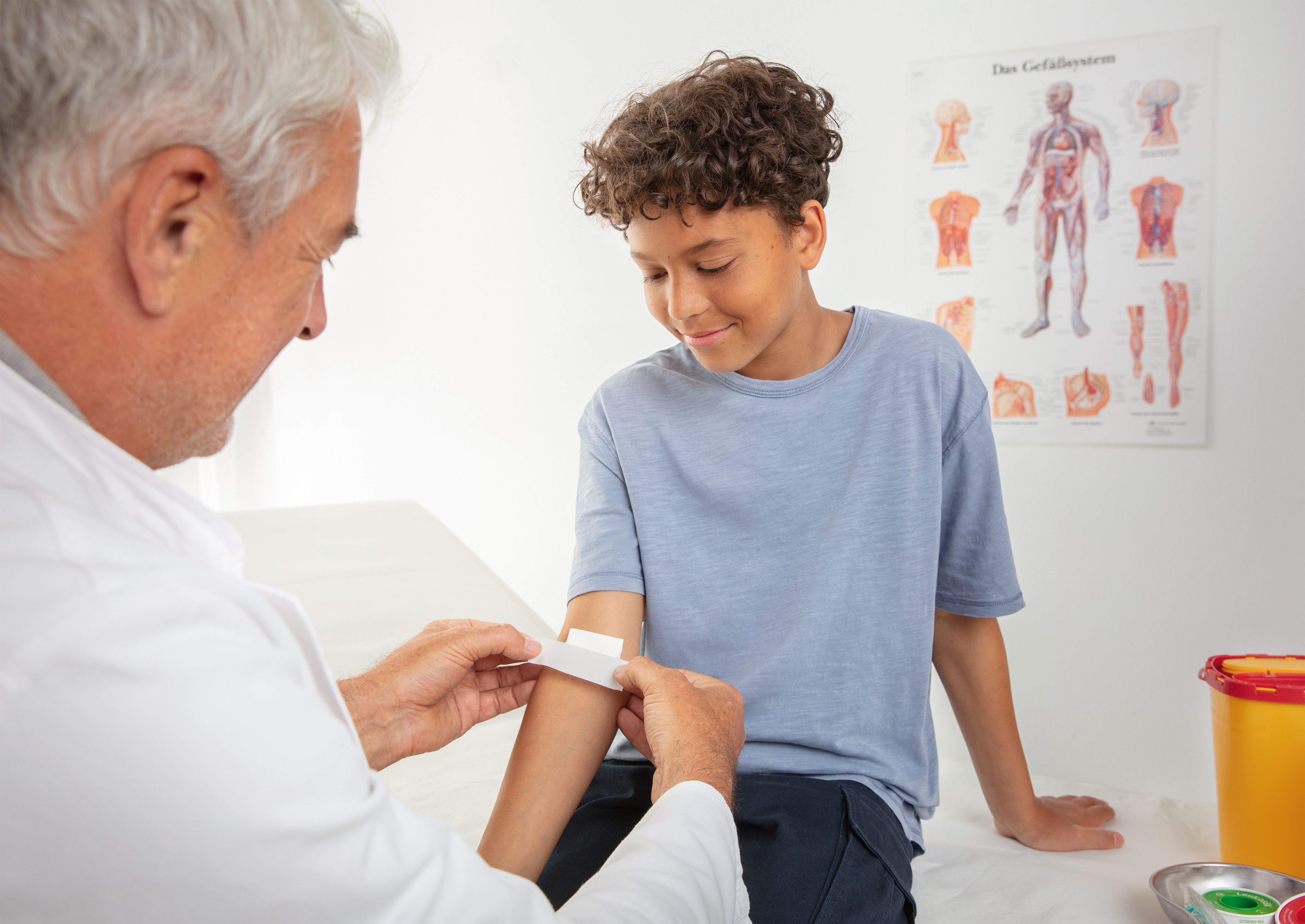 Un medico applica del nastro adesivo sul braccio di un ragazzo.