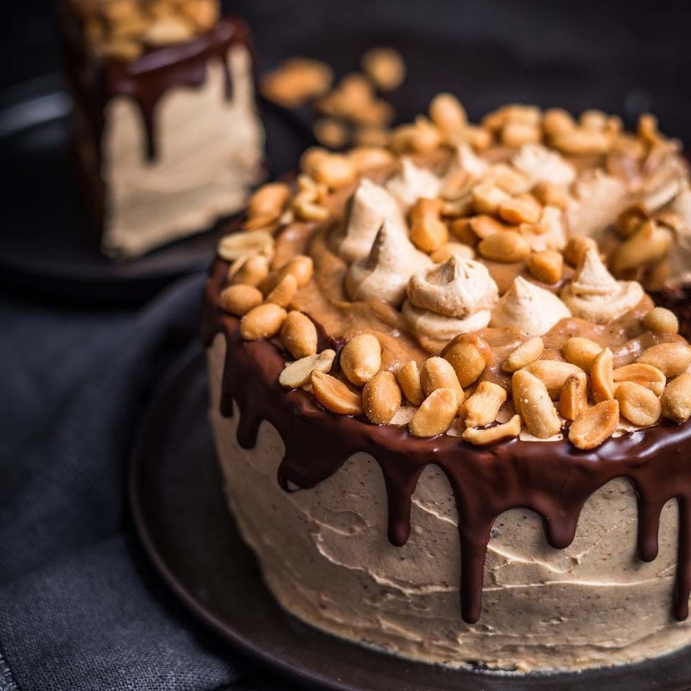 Torta con burro di arachidi e glassa al cioccolato. Guarnita con arachidi. Su un piatto.