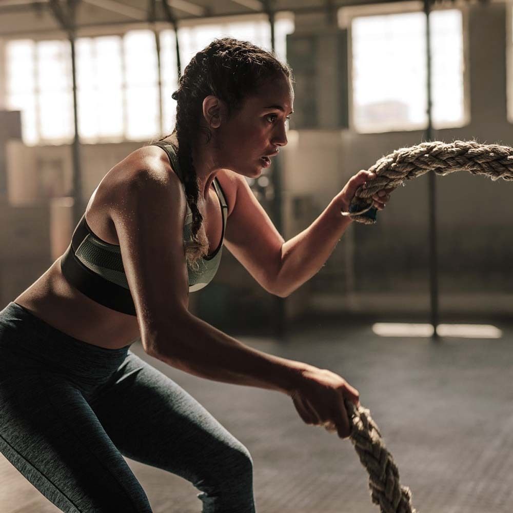 Donna che tira una corda in palestra. Abbigliamento sportivo, tiene una corda.