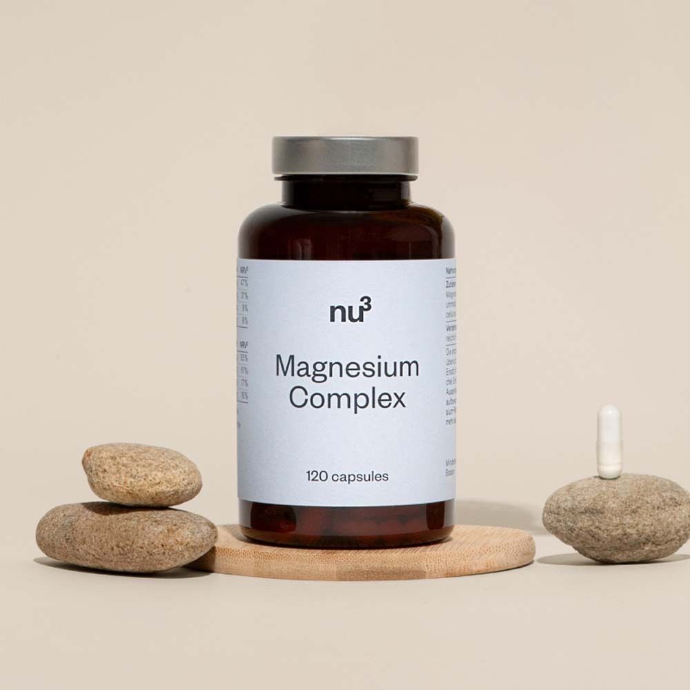 Flacone marrone con etichetta bianca « Magnesium Complex » e « 120 capsules ». Su una tavola di legno con pietre.